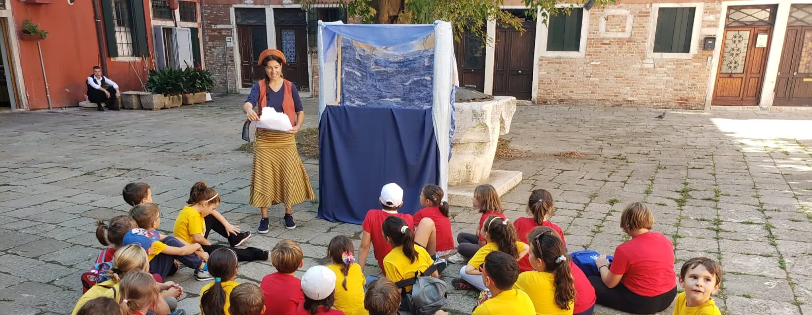 A group of children sitting in a Venetian square listening to a storyteller during a hunt